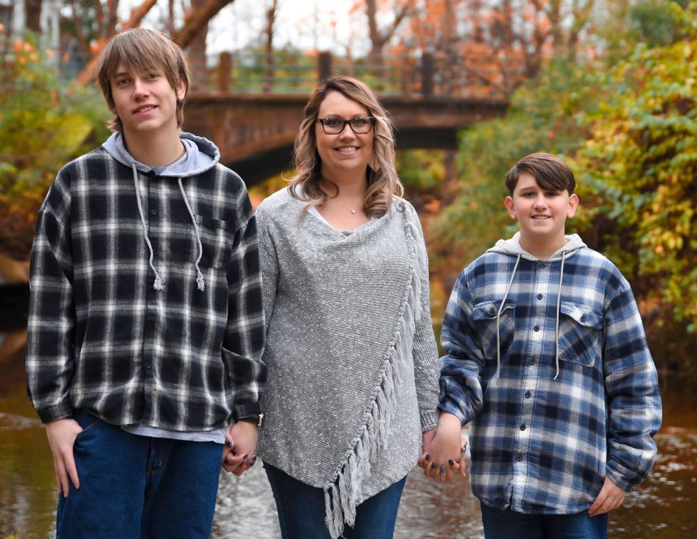 Family in matching plaid flannel shirts poses in front of autumn foliage near a covered bridge.