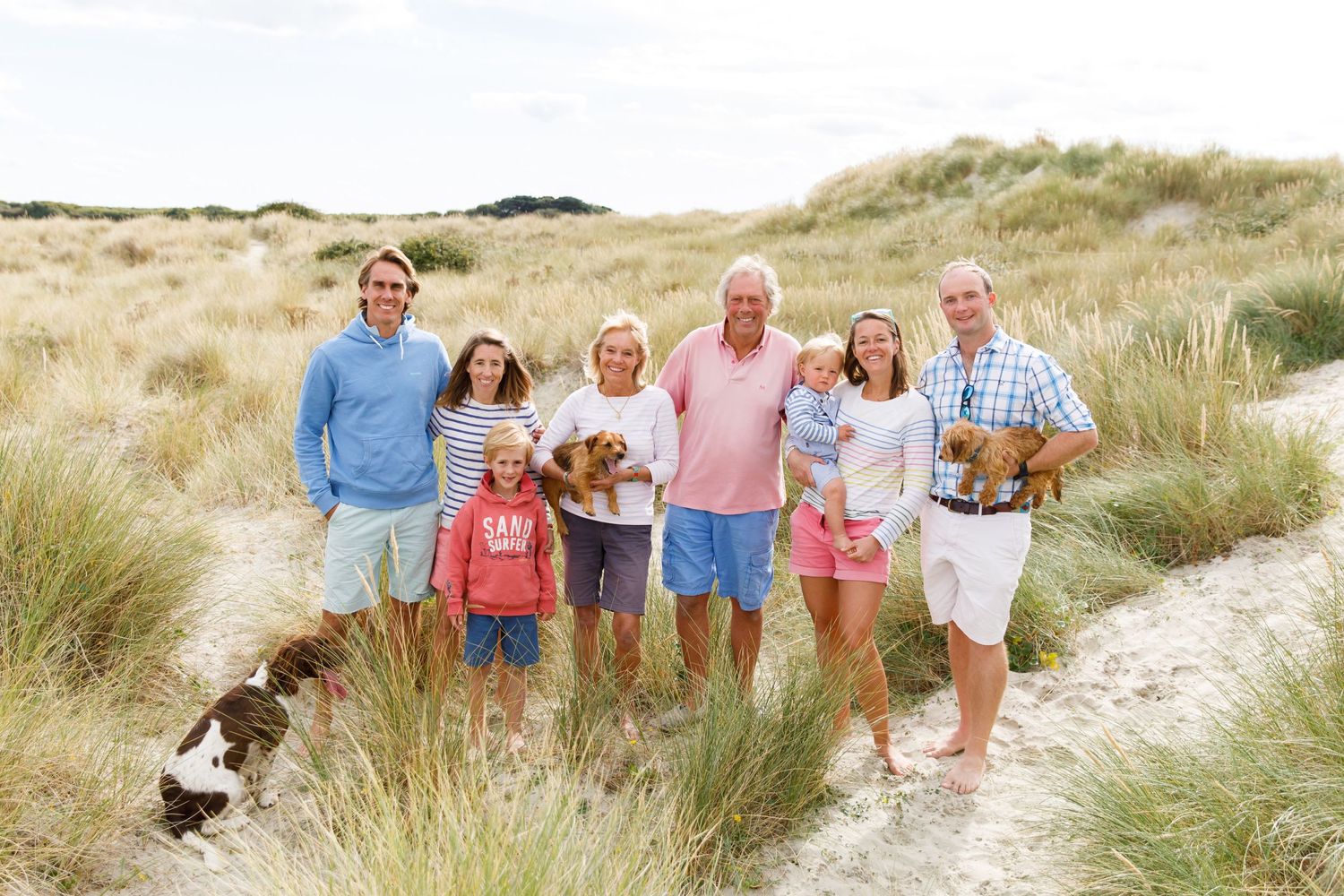 Group poses together on sandy beach path among coastal grass during a family beach photoshoot