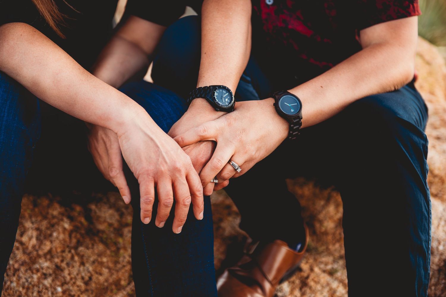 Close-up shot of hands wearing watches resting on knees in casual pose.