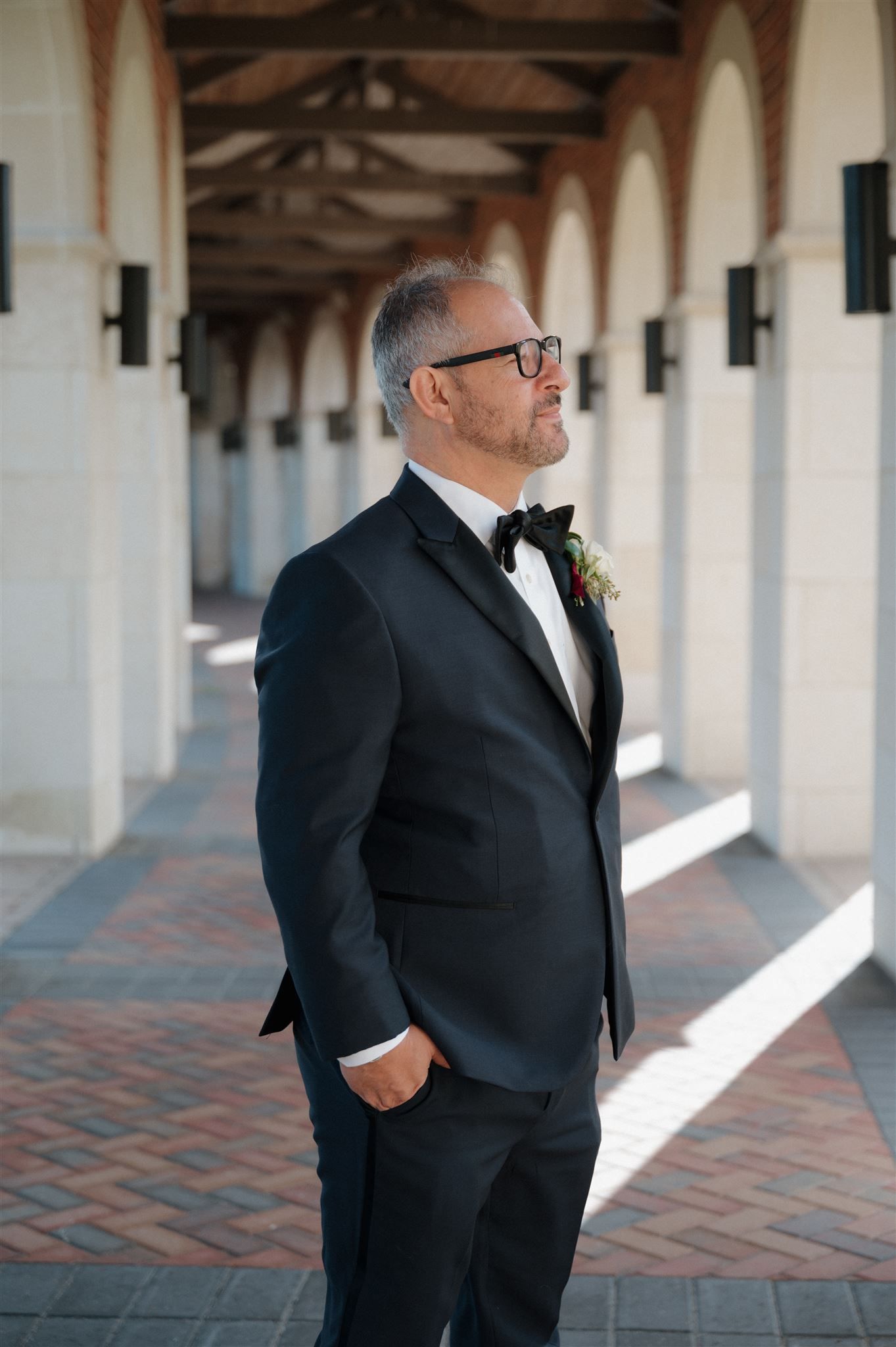 Classic wedding portrait of person in tuxedo standing in arched colonnade.