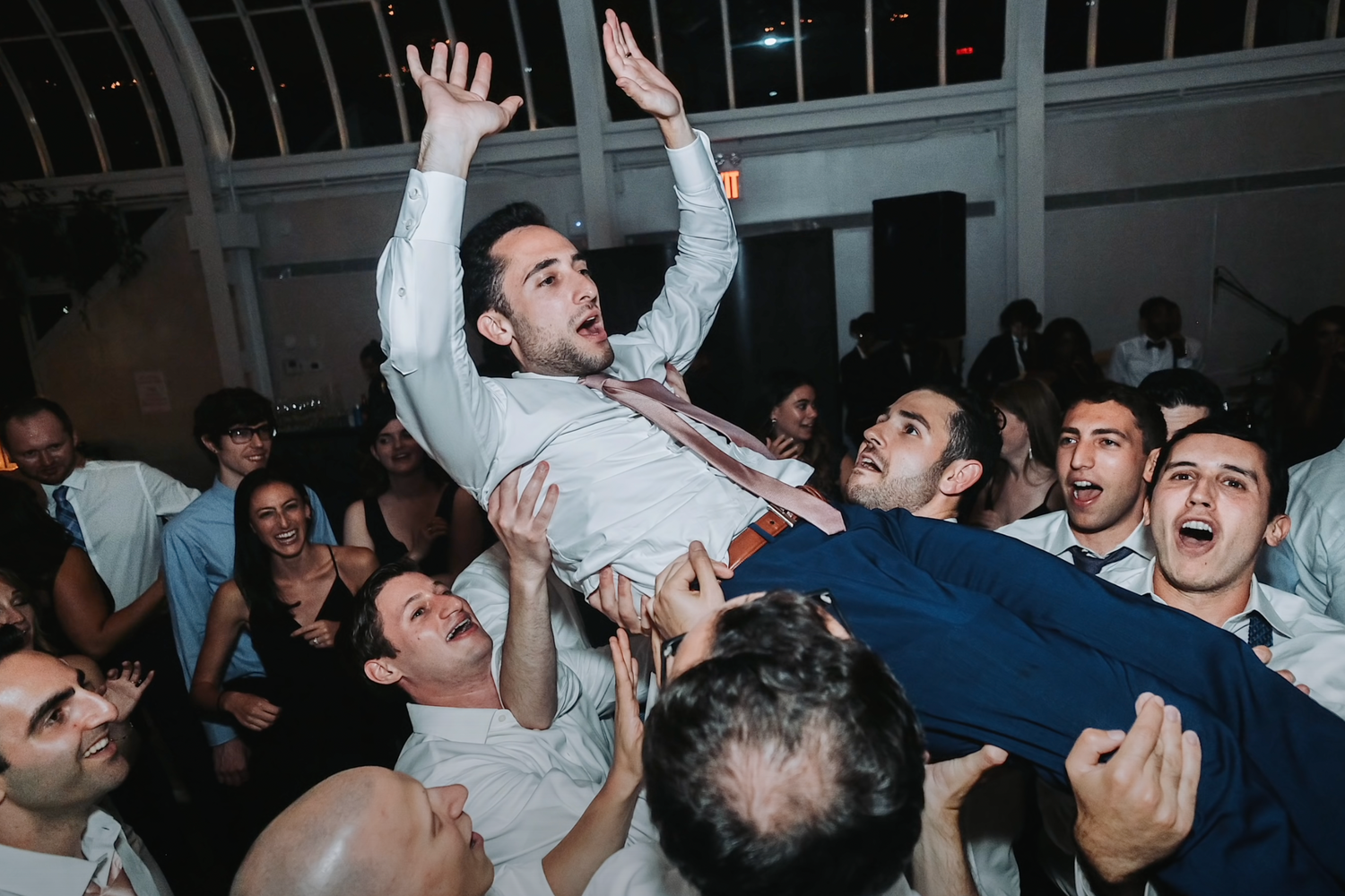 Wedding guests lift and celebrate with someone during an energetic reception party.