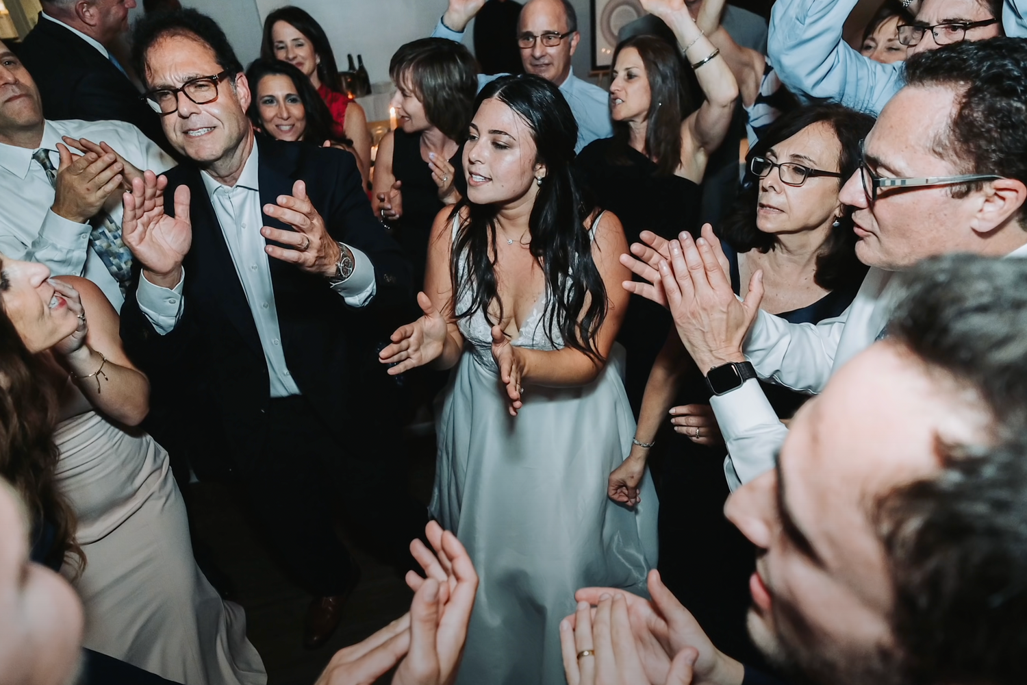 Wedding guests dancing and celebrating together at a dimly lit reception venue.