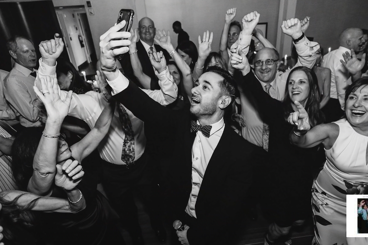 Black and white photo of wedding guests dancing and celebrating with raised arms.
