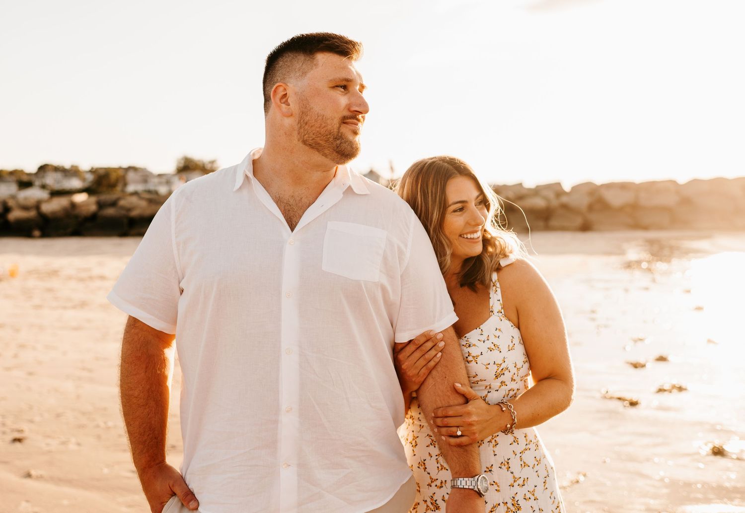 Couple in white outfits embracing on beach at sunset.