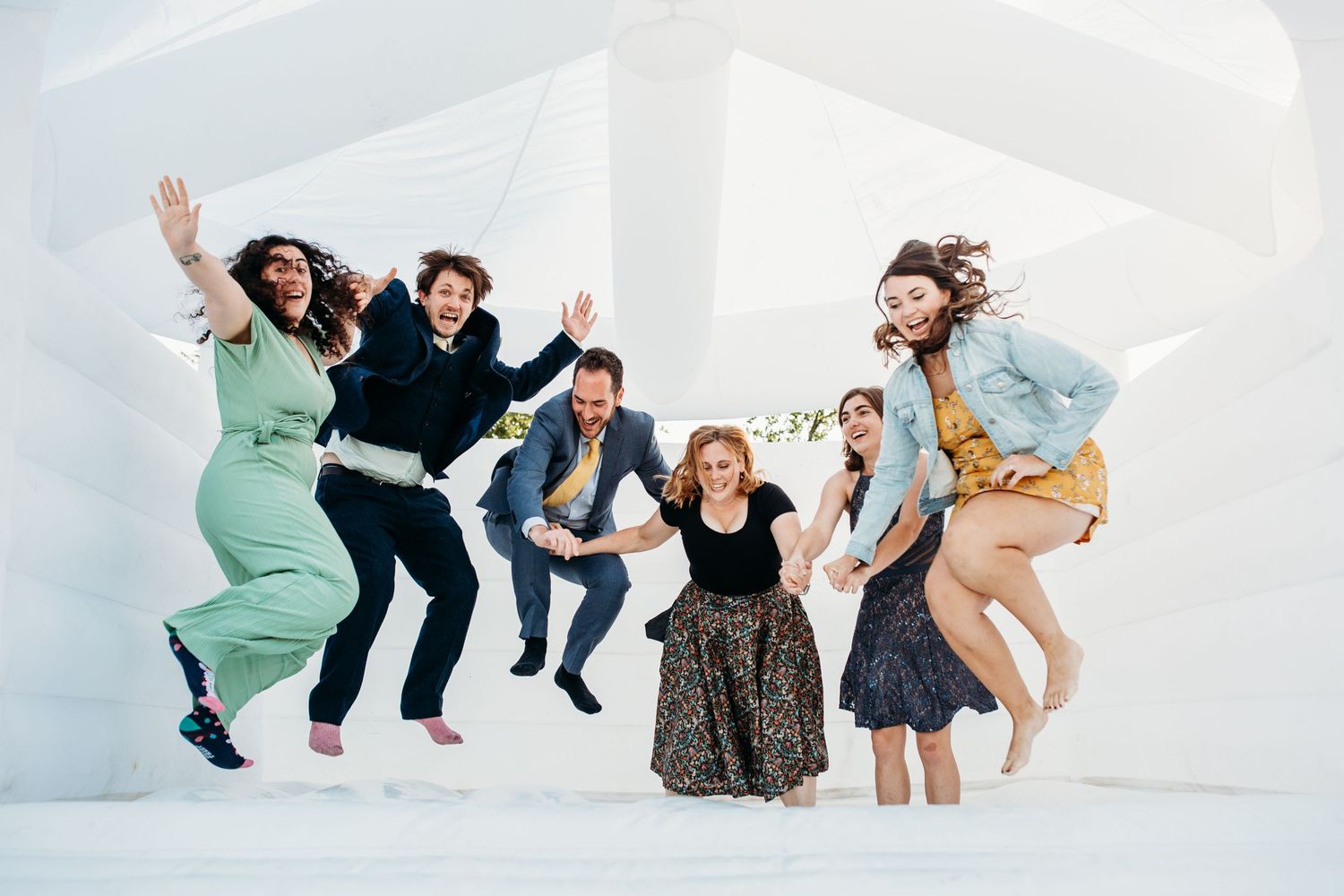 A group of people jump joyfully against a white wall during a celebratory moment.