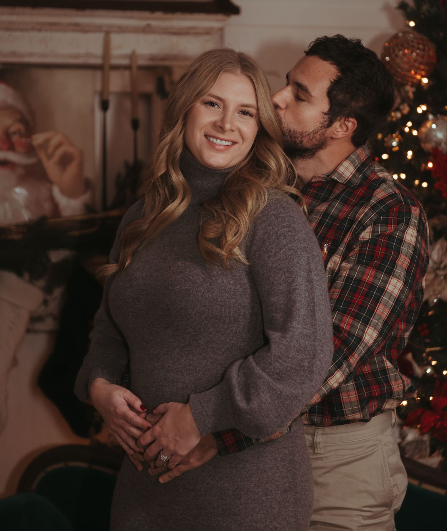 Cozy Christmas portrait of a couple embracing in front of a decorated tree in warm indoor lighting.