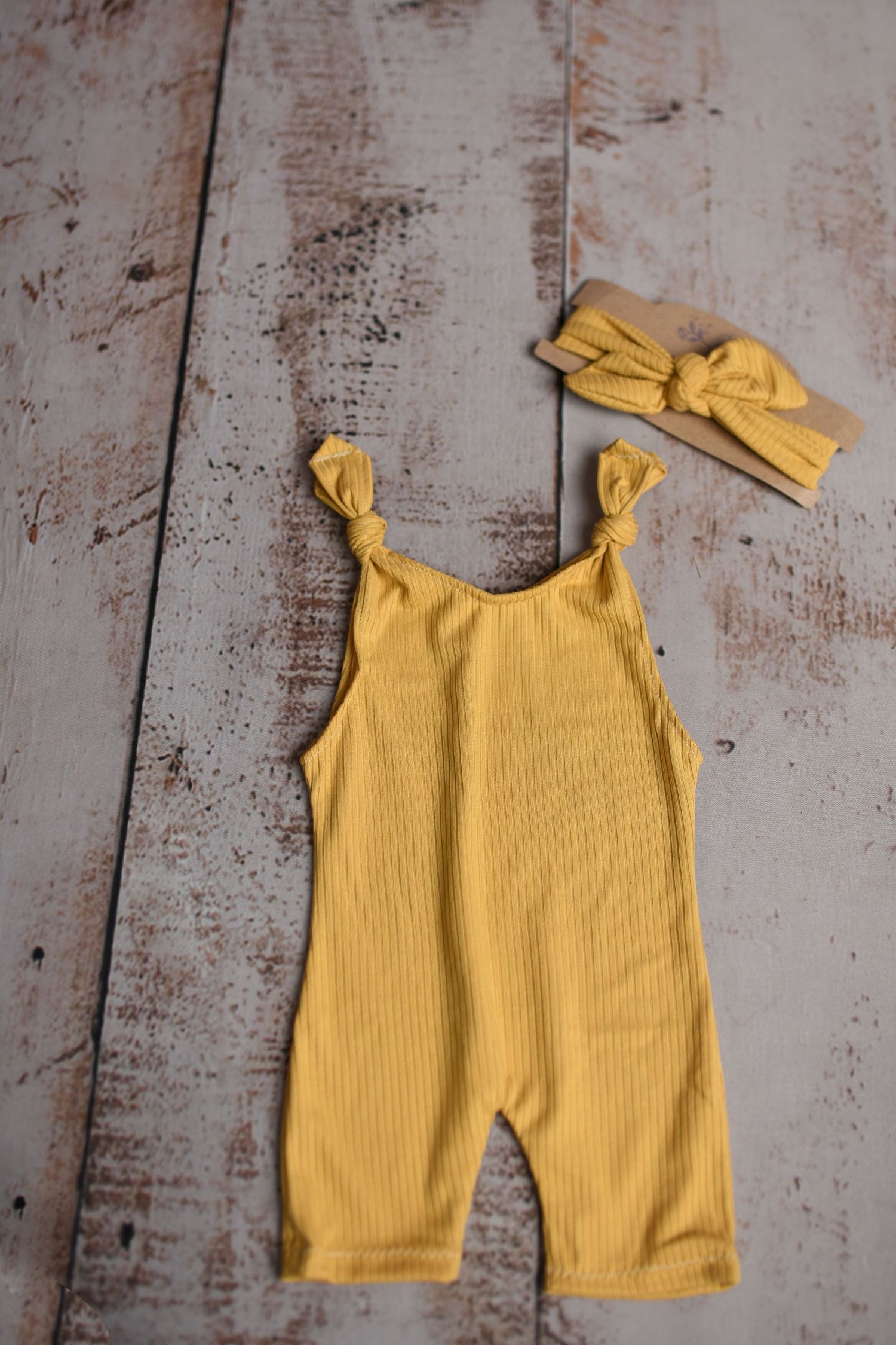 Yellow ribbed romper with bow straps laid flat on weathered wooden surface.