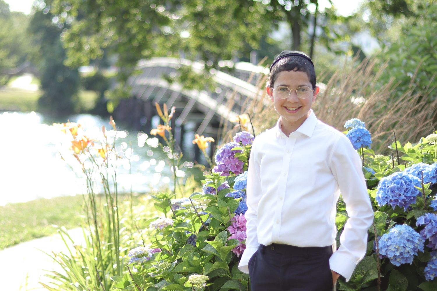 Young boy smiling in Divine Park, Spring Lake, NJ with a wooden bridge and colored flowers in the background
