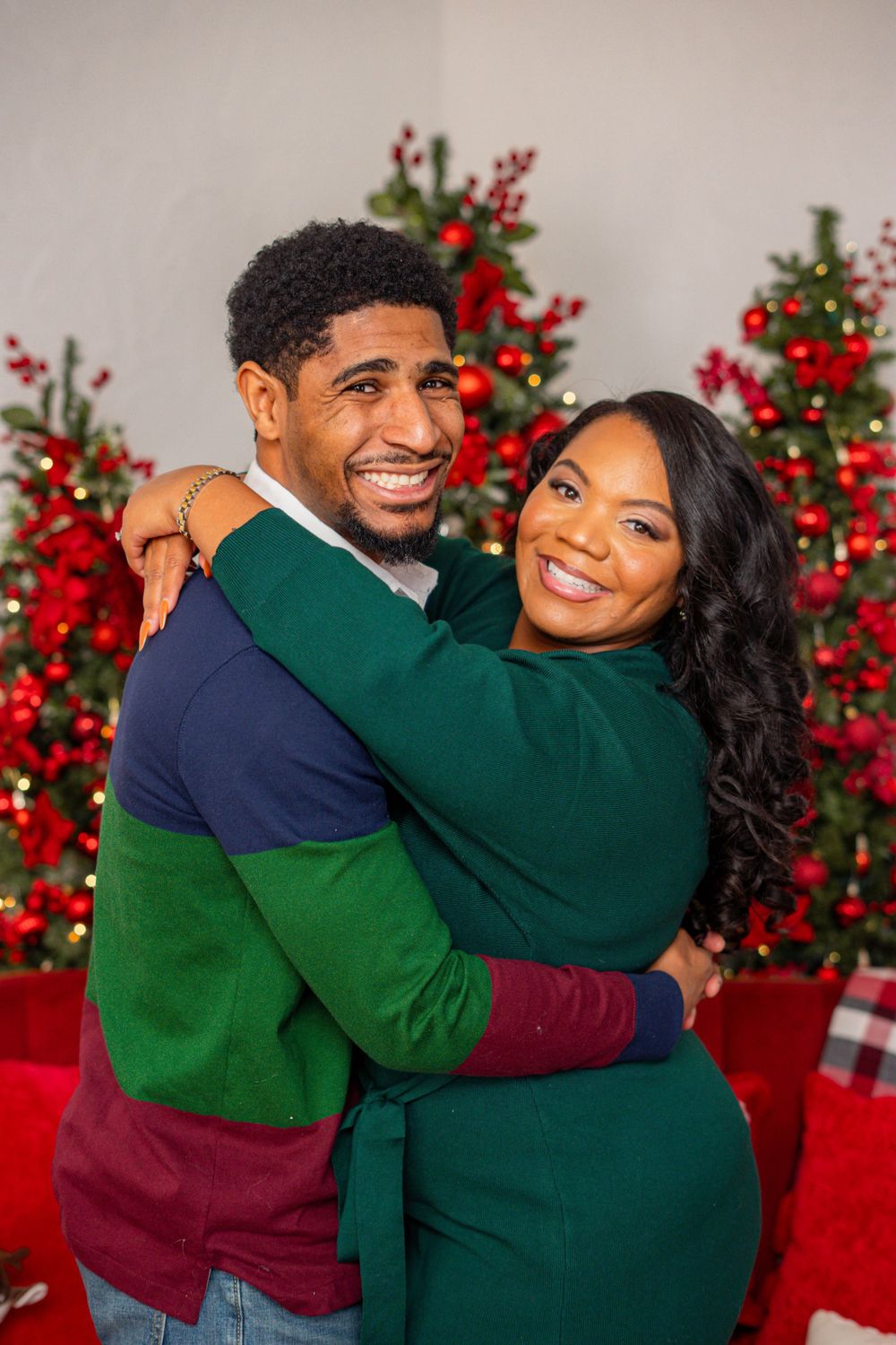 Smiling Black couple embracing each other in front of festive red Christmas trees.