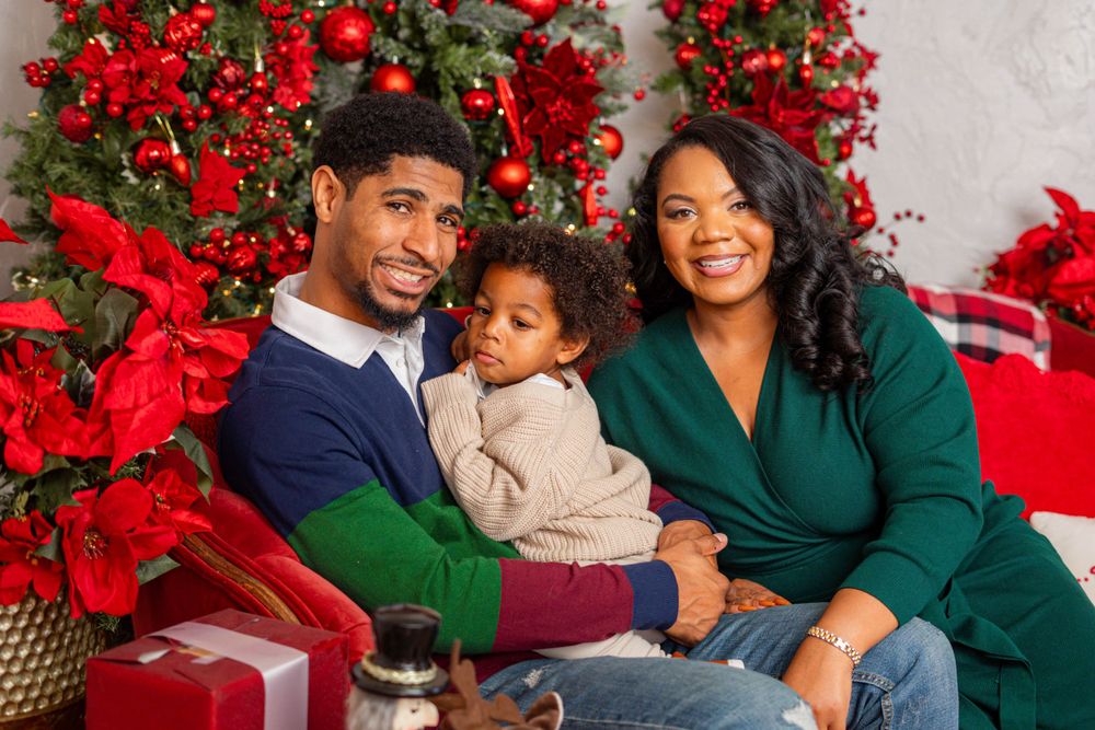Happy Black family with toddler posing together in front of a decorated Christmas tree.