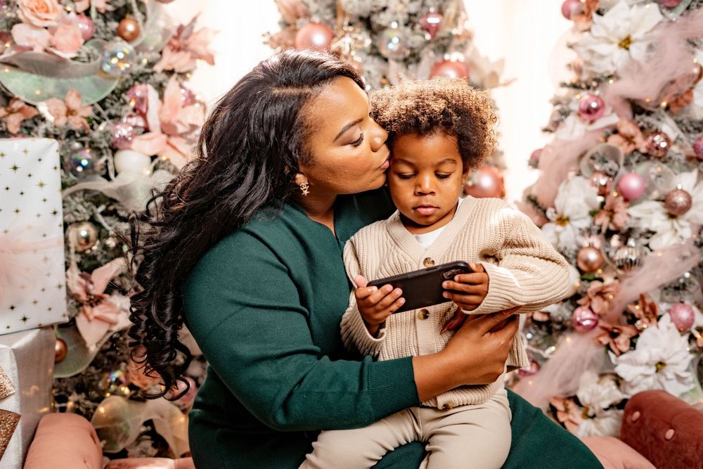 Loving mother kissing her young child while sitting in front of decorated Christmas trees.