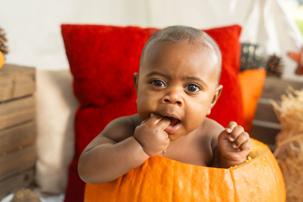 Adorable baby sitting inside a large orange pumpkin during a fall Halloween photo session.