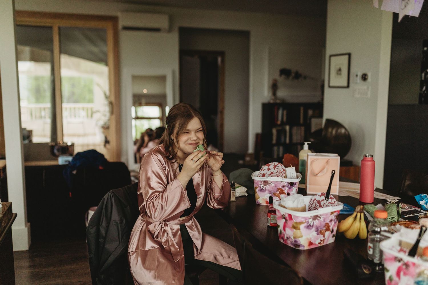 Wedding preparations with a pink silk robe and wrapped gifts on a wooden table at a rustic venue.