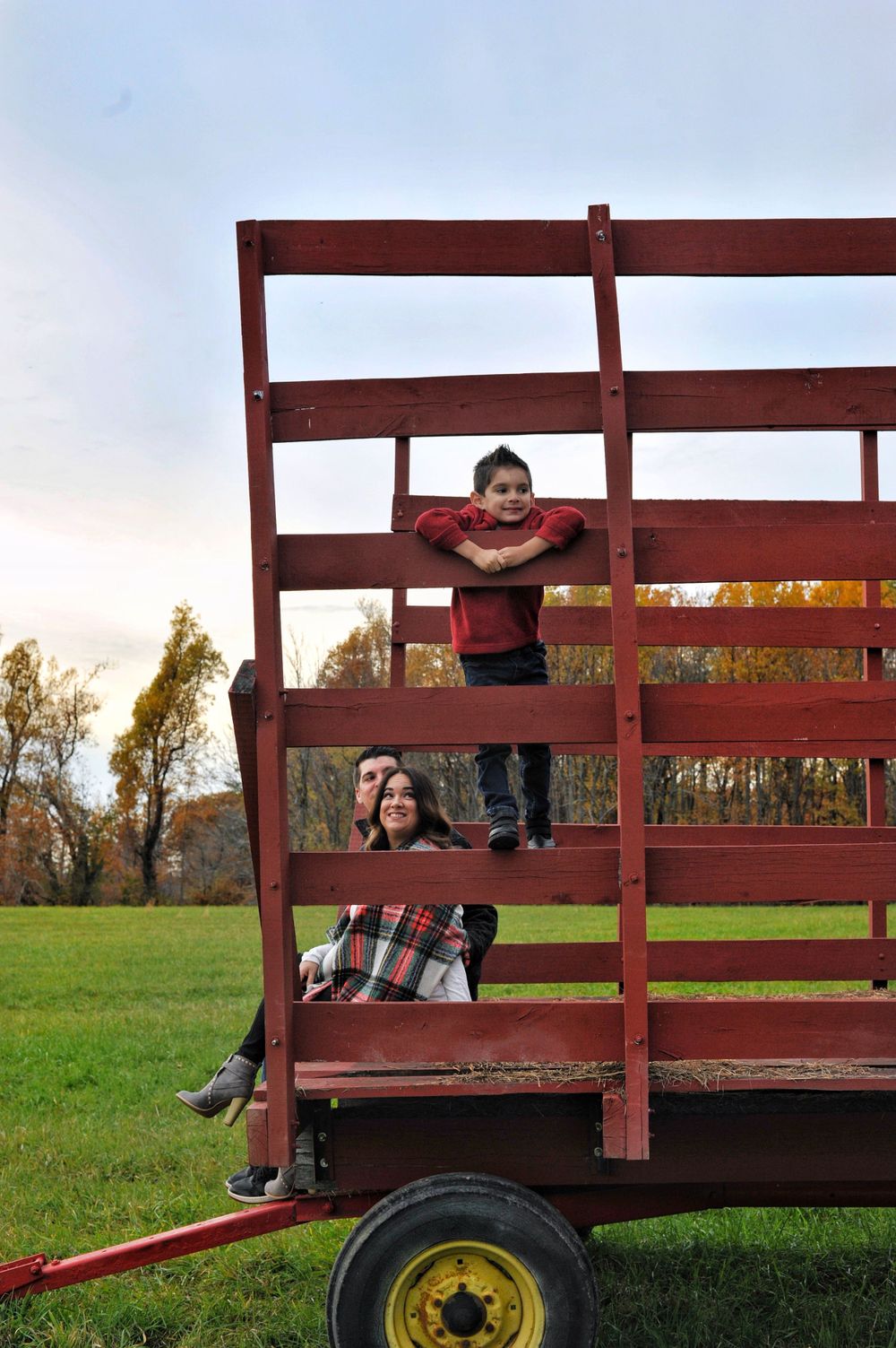Boy portrait on hay wagon with mom and dad looking, fall foilage field