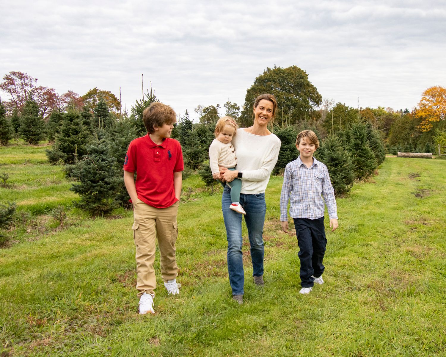A family walks together between evergreen trees at a Christmas tree farm on an autumn day.