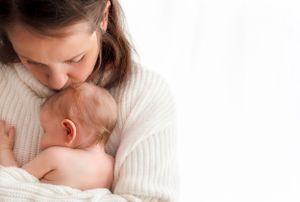 Mother lovingly kisses top of baby's head as her newborn snuggles into her cozy sweater