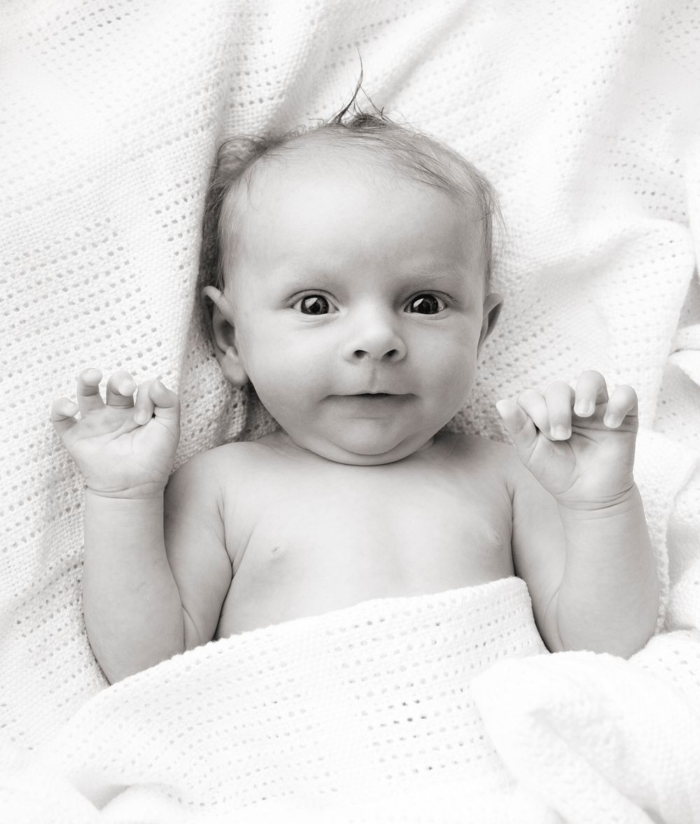 wide eyed little baby wiggles his fingers out of the blanket