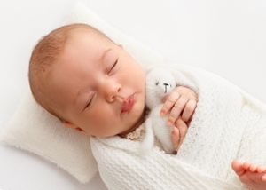 newborn baby lays on a tiny pillow and holds a tiny teddy bear