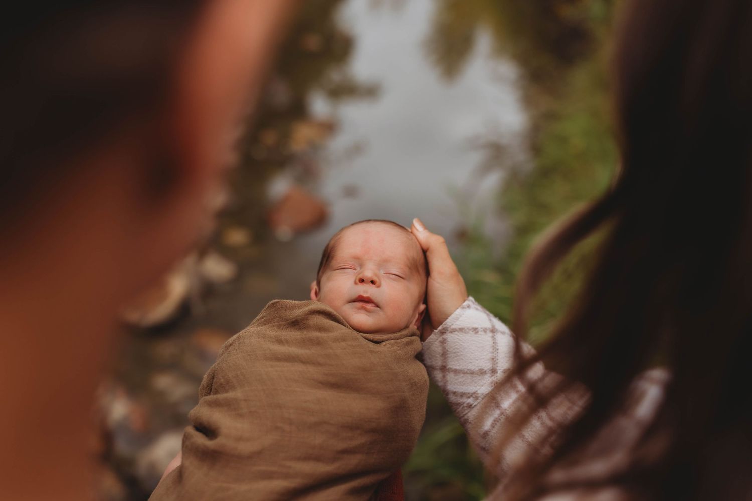 Sleeping newborn baby wrapped in brown swaddle blanket during an outdoor photoshoot.