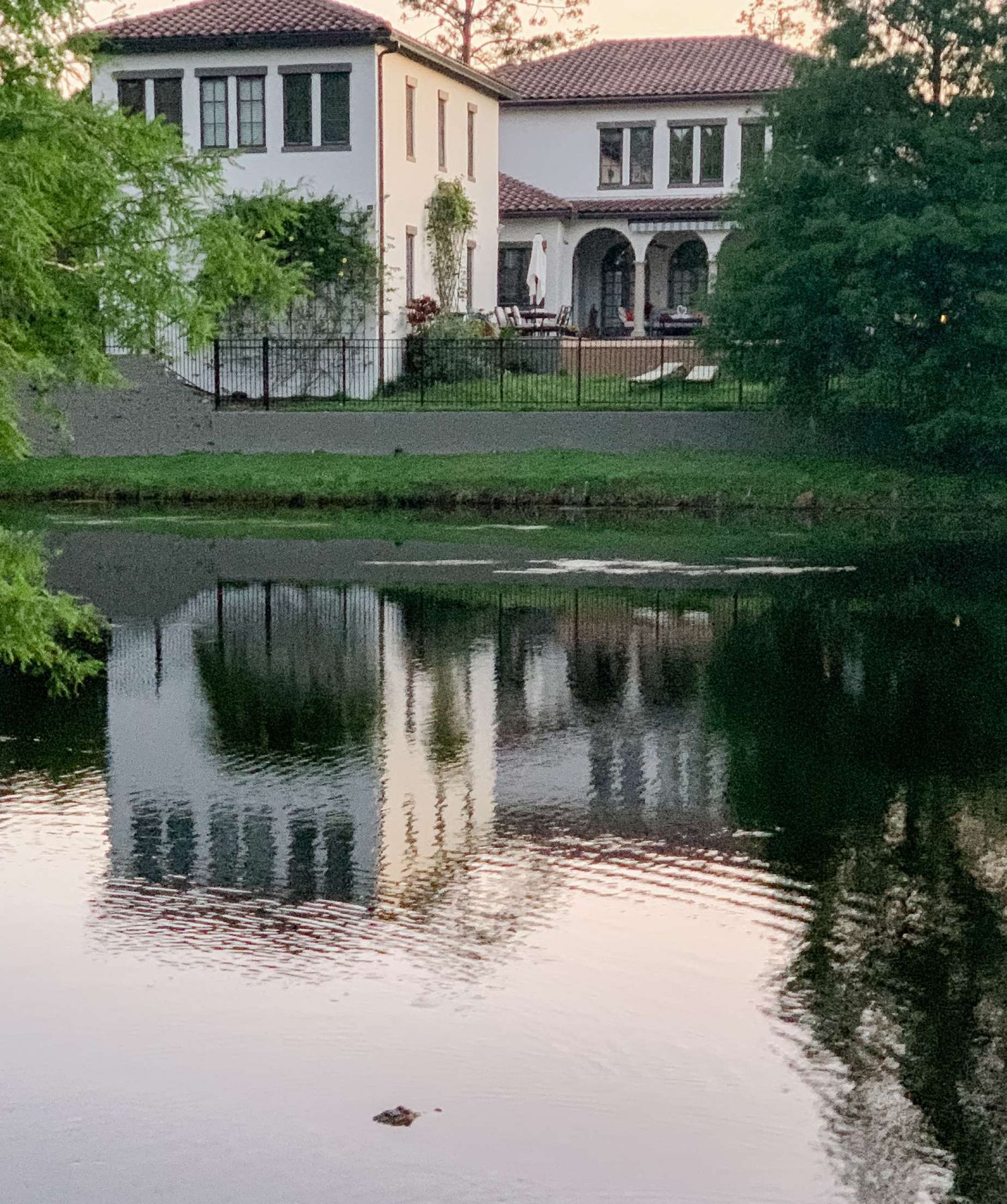 Mediterranean-style villa with cream walls and terracotta roof reflects in a tranquil pond.