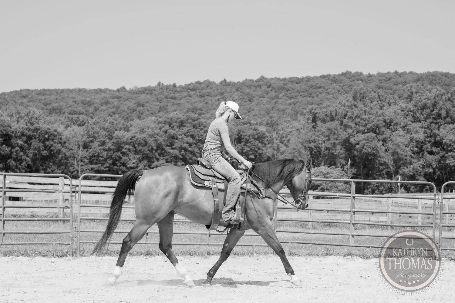 Black and white photo of equestrian training session in outdoor arena with mountain backdrop.