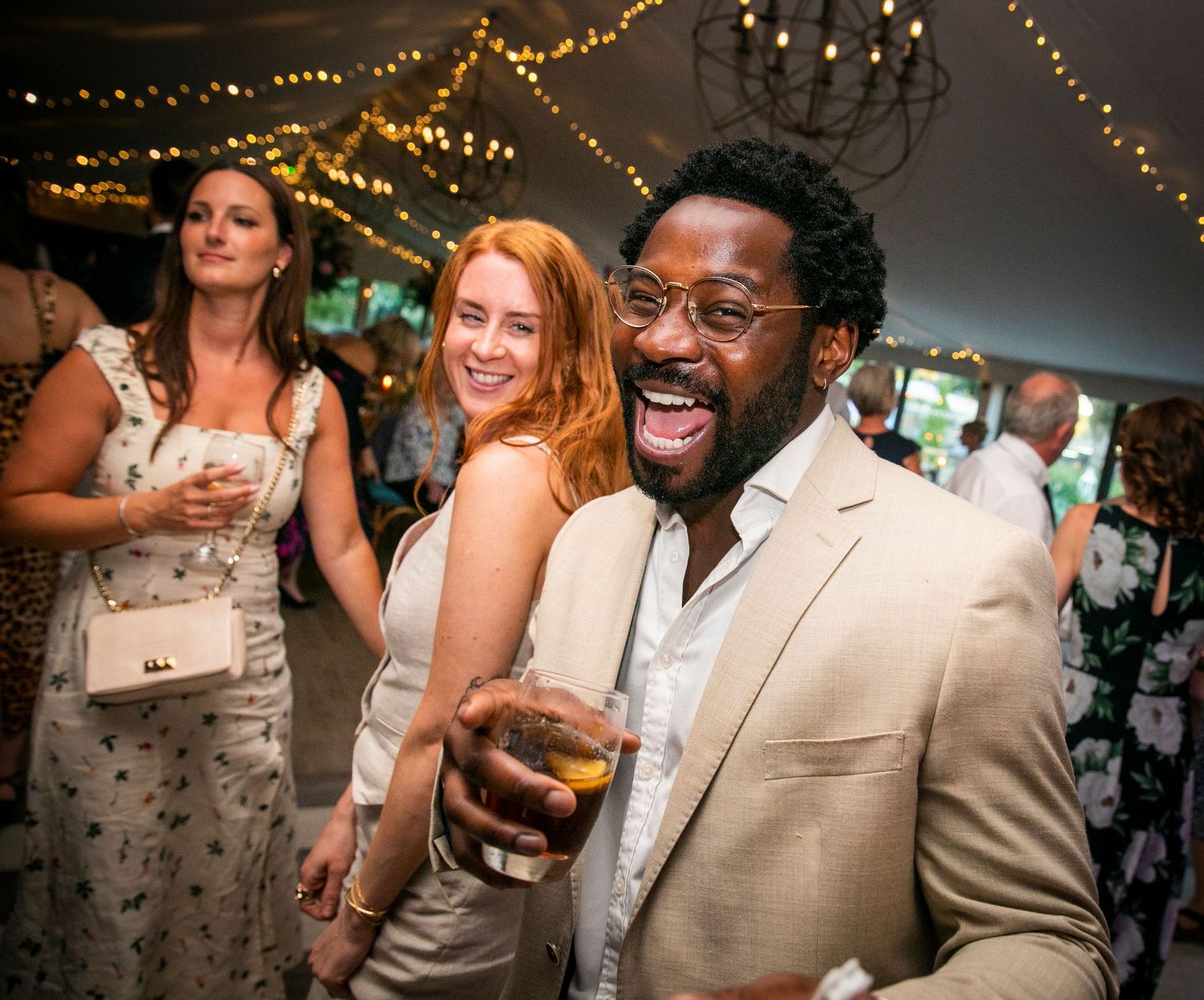 Wedding party guests enjoying themselves at a reception with string lights overhead.