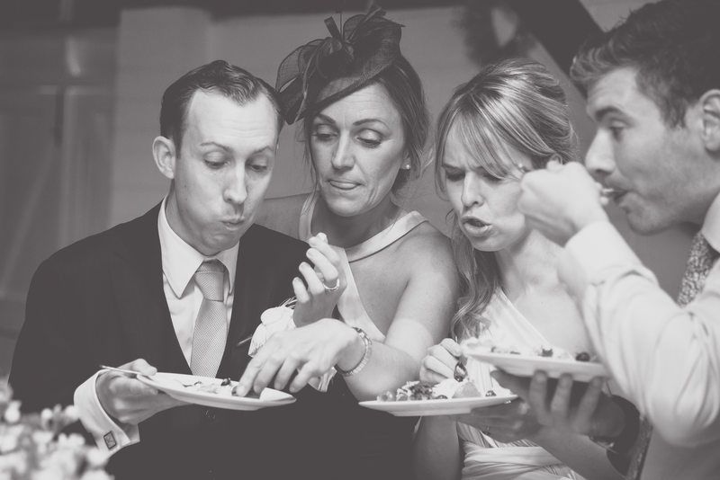 Wedding guests blow out candles together while enjoying dessert at reception table.