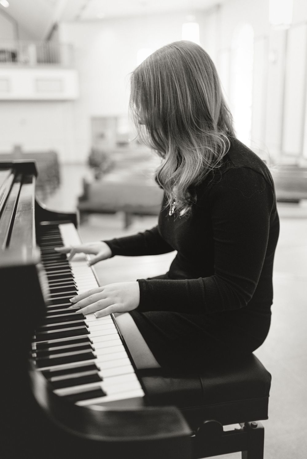 Black and white image of someone playing piano in a bright interior space.