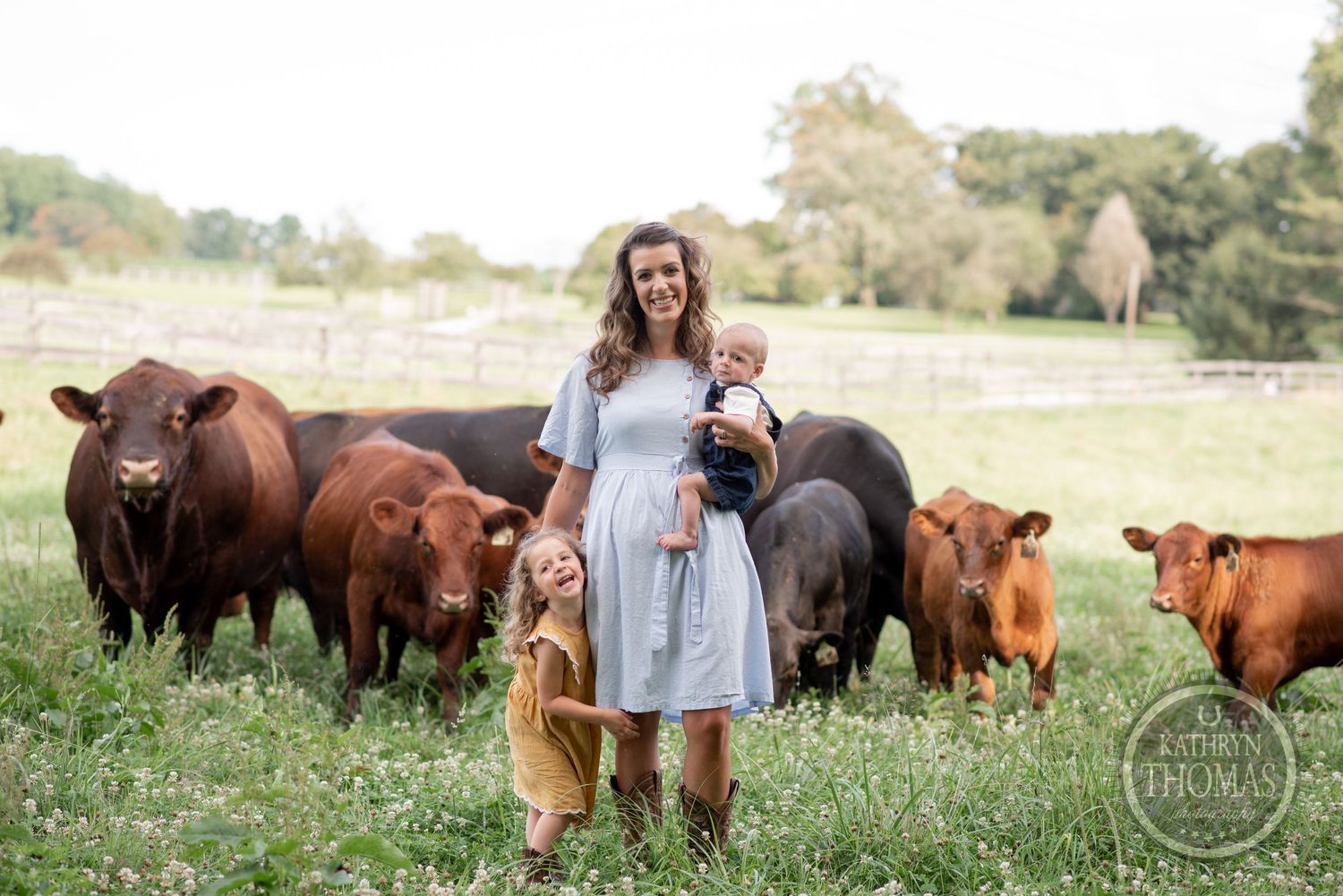 Farm family standing in a field with their herd of brown and black cattle.