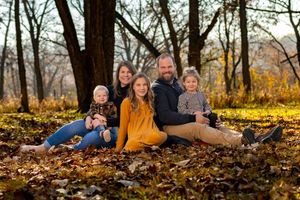 Family group sitting together on autumn leaves in a wooded area during golden hour.