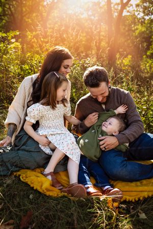 A family shares tender moments together while relaxing on a yellow blanket in a sunlit garden setting.