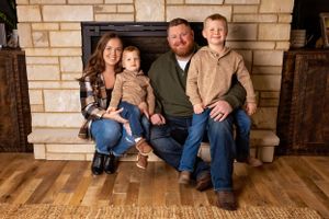 A family sits together on a wooden floor against a light brick fireplace backdrop for a warm indoor portrait.Janesville, WI
Brodhead, WI
