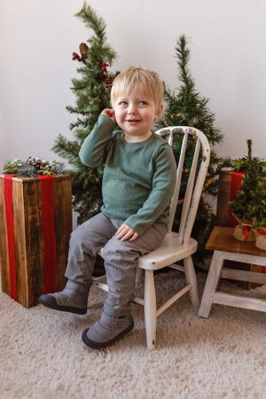 Small child sits on white chair next to Christmas tree and wrapped presents in festive holiday scene.Janesville, WI
Brodhead, WI