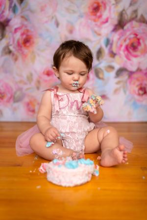 A small child in a pink lace romper enjoys smashing and playing with a birthday cake against a floral backdrop.Janesville, WI
Brodhead, WI