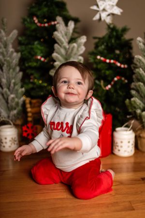 A small child in a red and white holiday outfit sits smiling by decorated Christmas trees and festive decor.Janesville, WI
Brodhead, WI