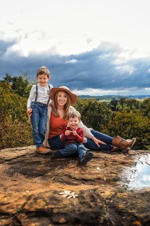 A family sits together on a rocky outcrop against a dramatic cloudy sky during an outdoor photo session.