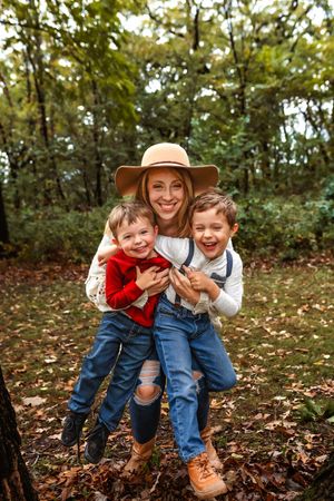 A playful autumn scene showing people in casual attire having fun among fallen leaves in a wooded setting.