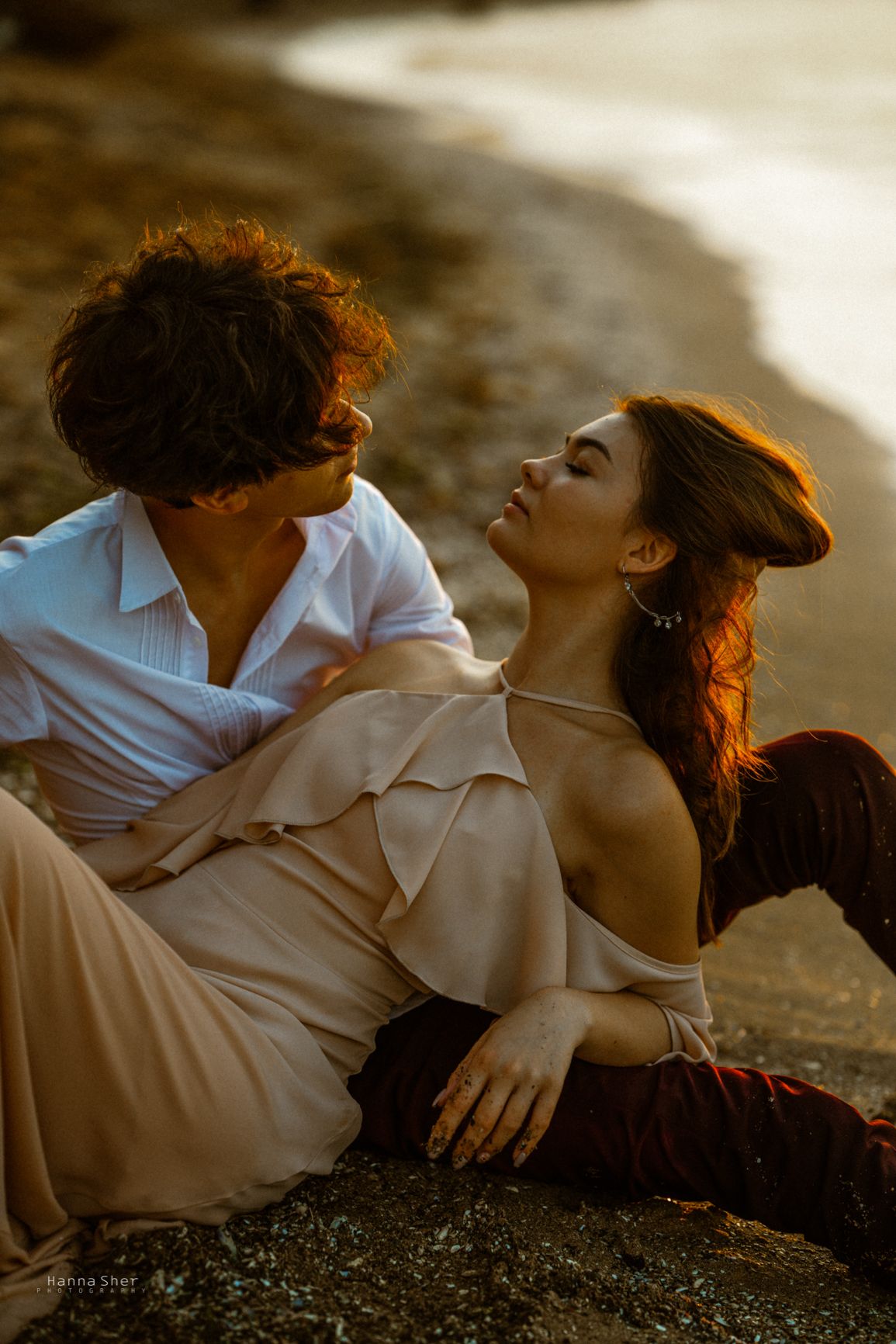 Romantic couple sharing an intimate moment while sitting together on a sunlit beach at sunset.
