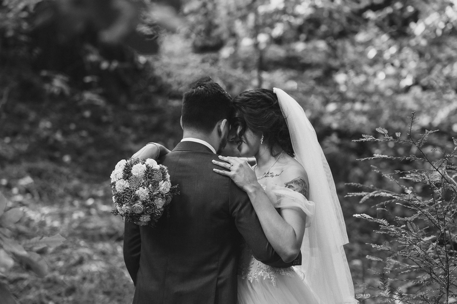 A romantic black and white portrait of a couple embracing in a forest setting.
