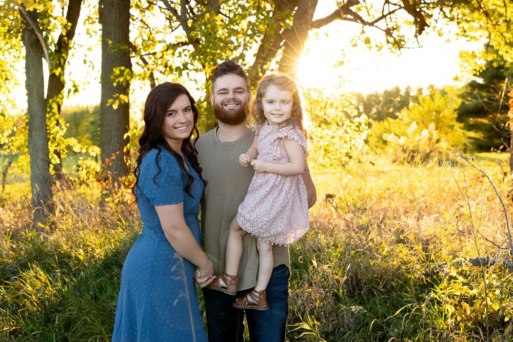 Natural family portrait at sunset with golden backlight filtering through trees.