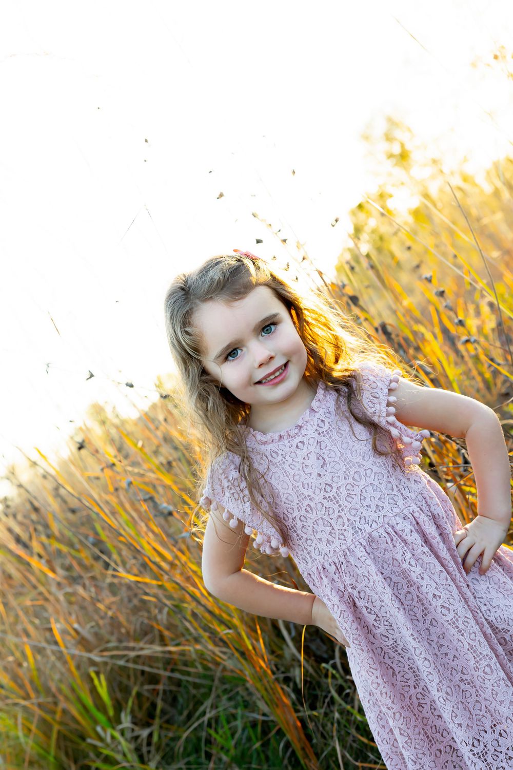 Sweet portrait of a child in a pink lace dress posing against golden wheat at sunset.
