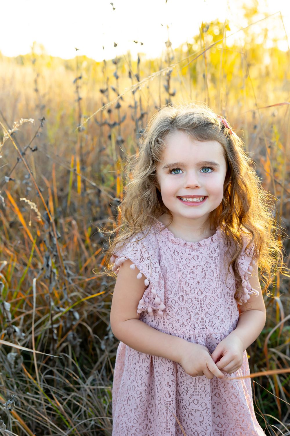 Joyful portrait of a young child in pink lace dress with sunlit field background.