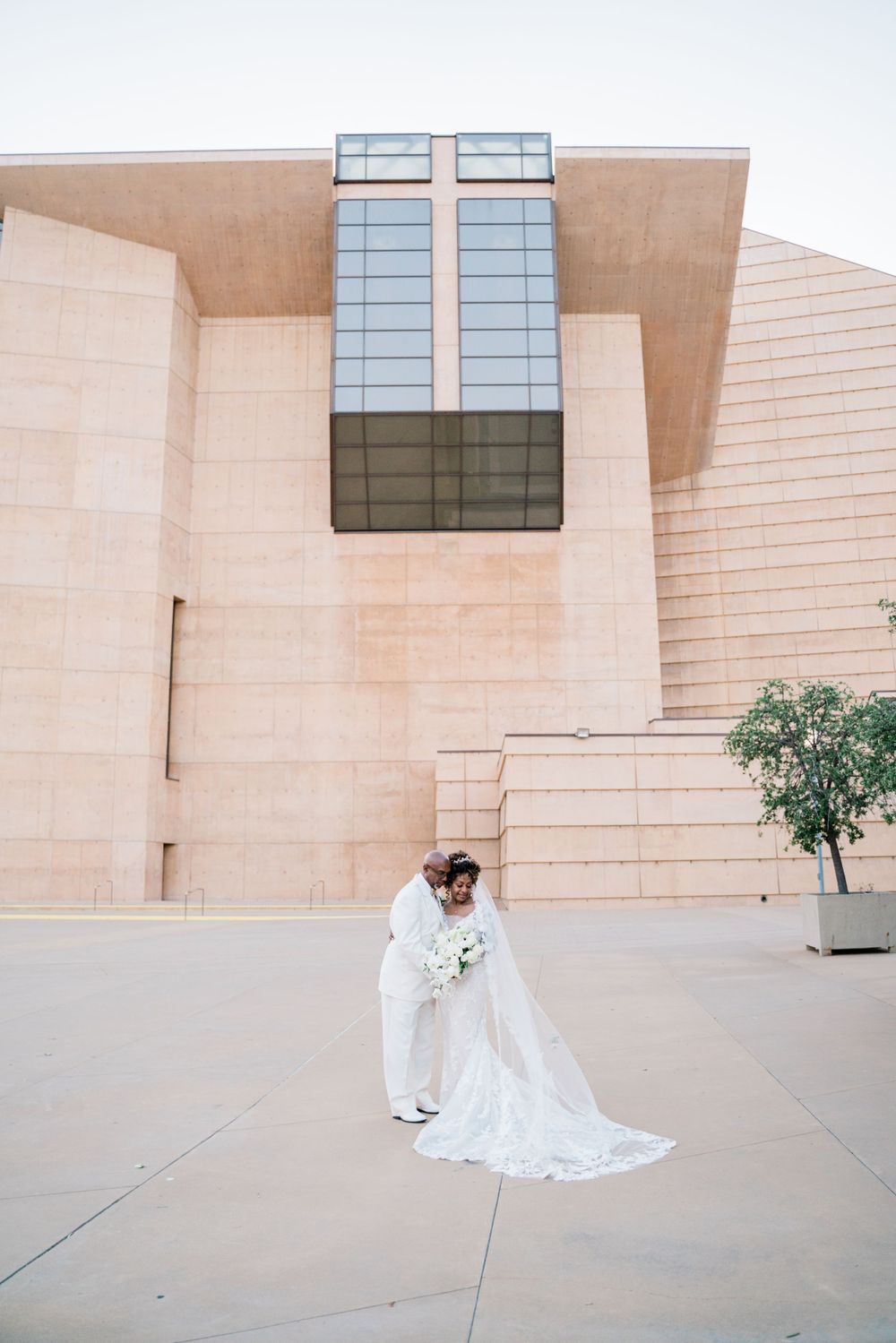 Wedding portraits against modern architectural backdrop with beige stone walls and glass windows.