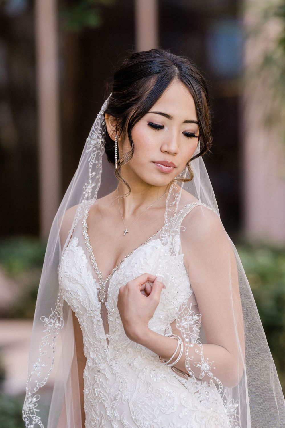 Bride in detailed lace gown and veil poses with eyes closed in elegant portrait.