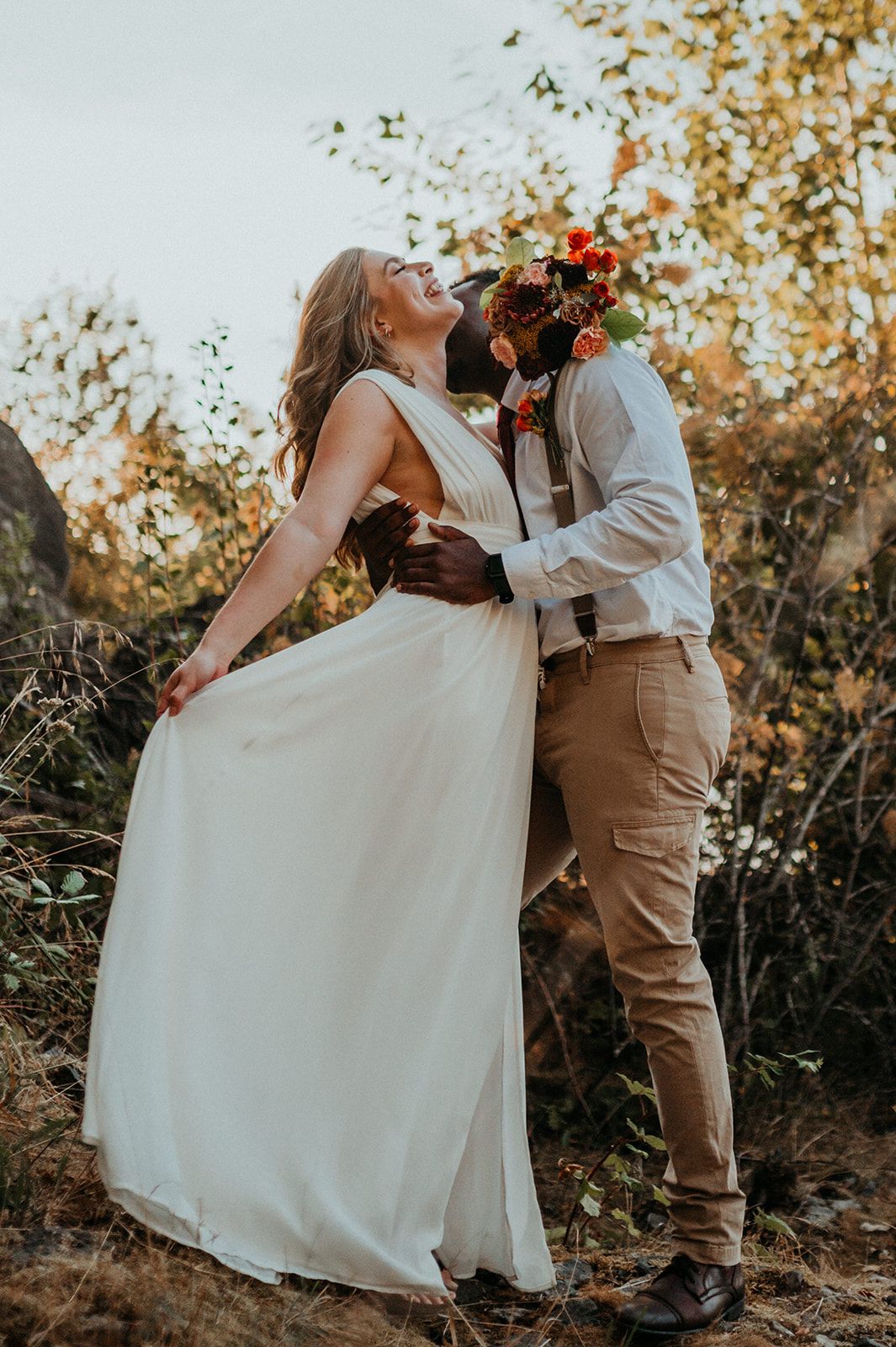 Couple in wedding dress and khaki suit dancing on cliff edge surrounded by fall colors.