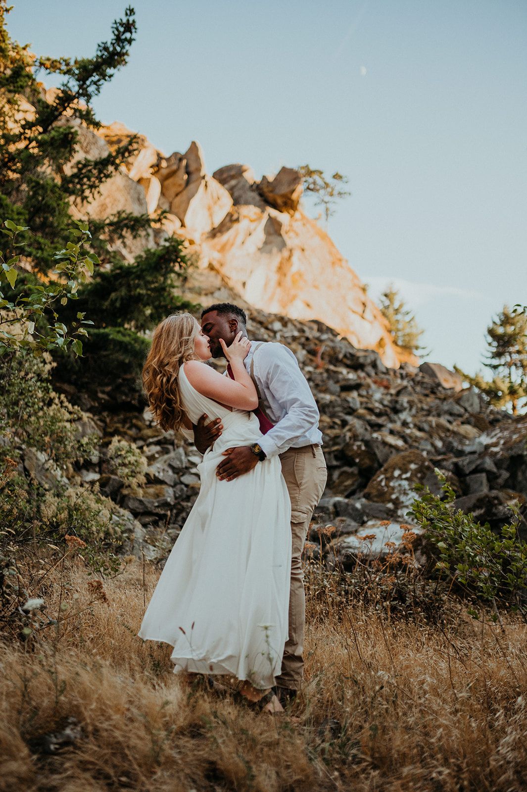 Newlyweds share an intimate moment against a scenic mountain backdrop at sunset.