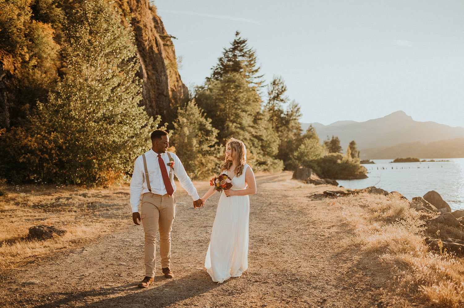 Couple walks hand in hand along a scenic mountain path during golden hour.