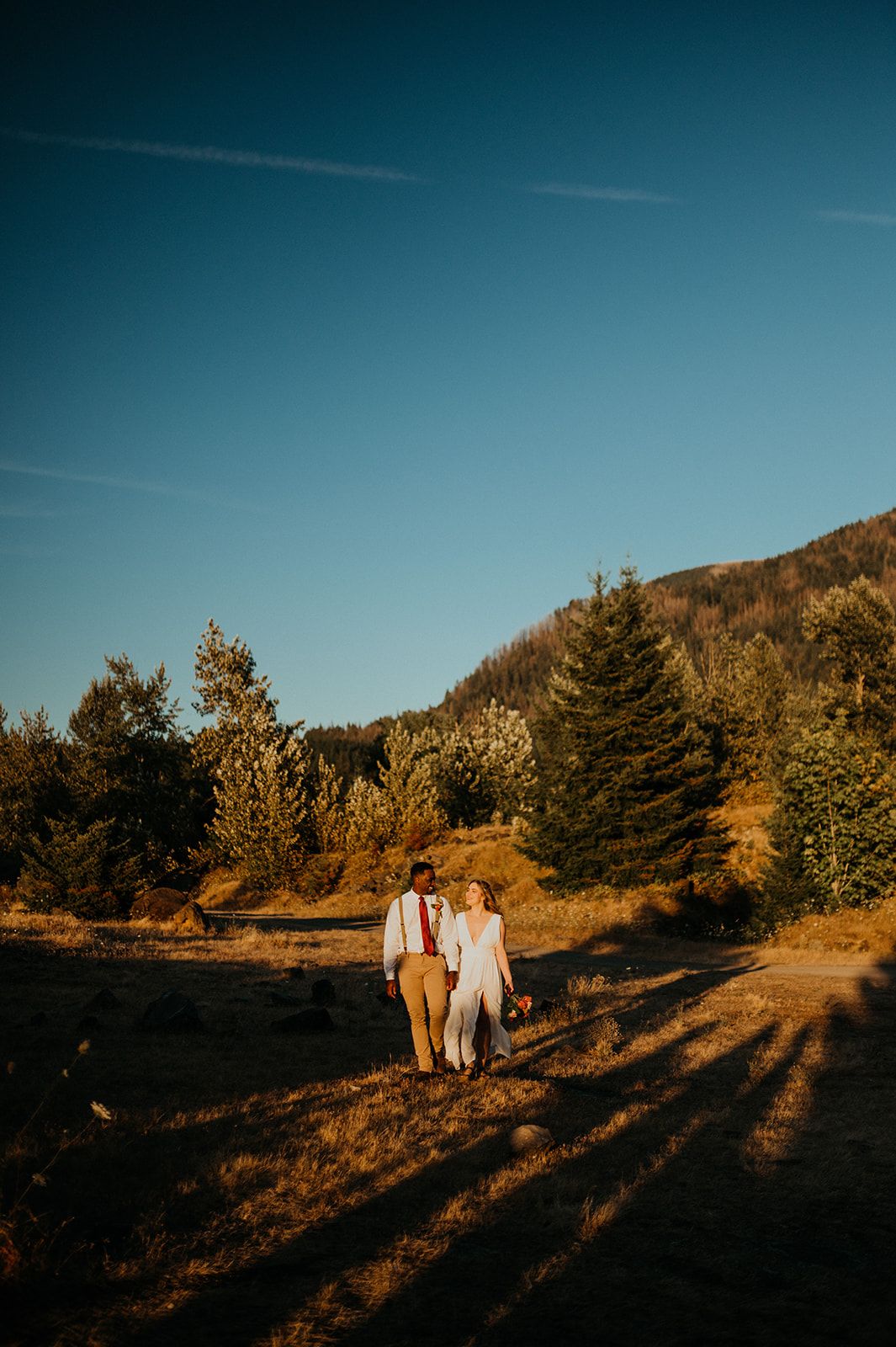 Silhouetted couple walks along mountain ridge during late afternoon golden light.