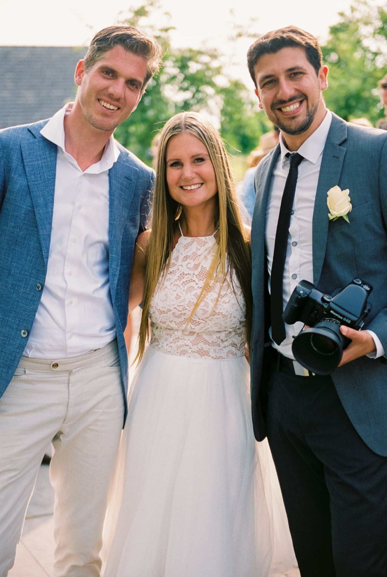 Wedding party members pose outdoors in formal attire on a sunny day.