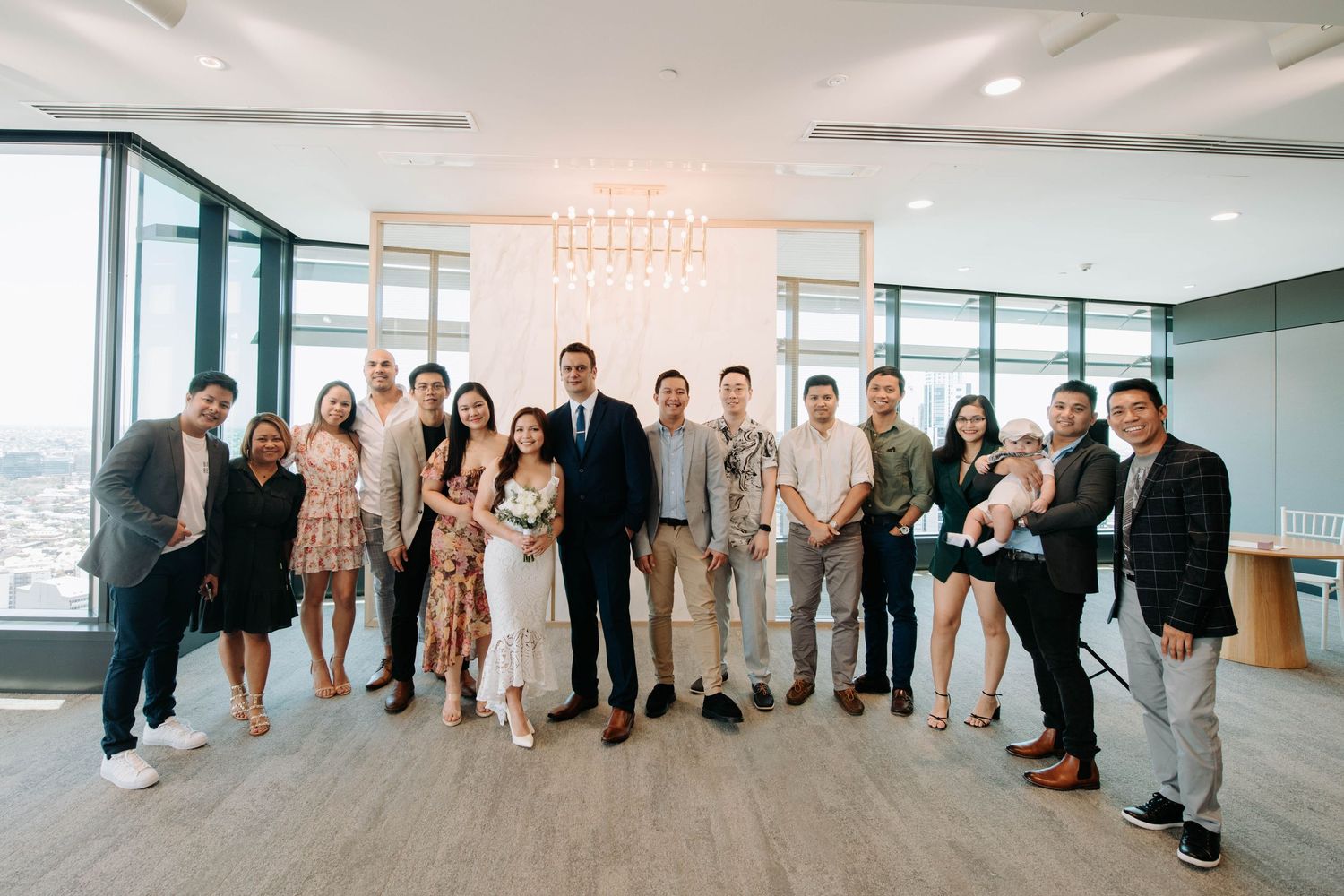 Wedding party group photo with guests in formal attire in modern bright venue.